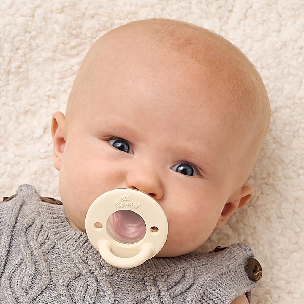 Newborn in a grey knit with the cream Itzy Ritzy shield and a clear nipple visible